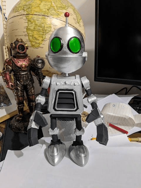 Clank — a small silver desk robot with green eyes, standing on papers in front of a globe